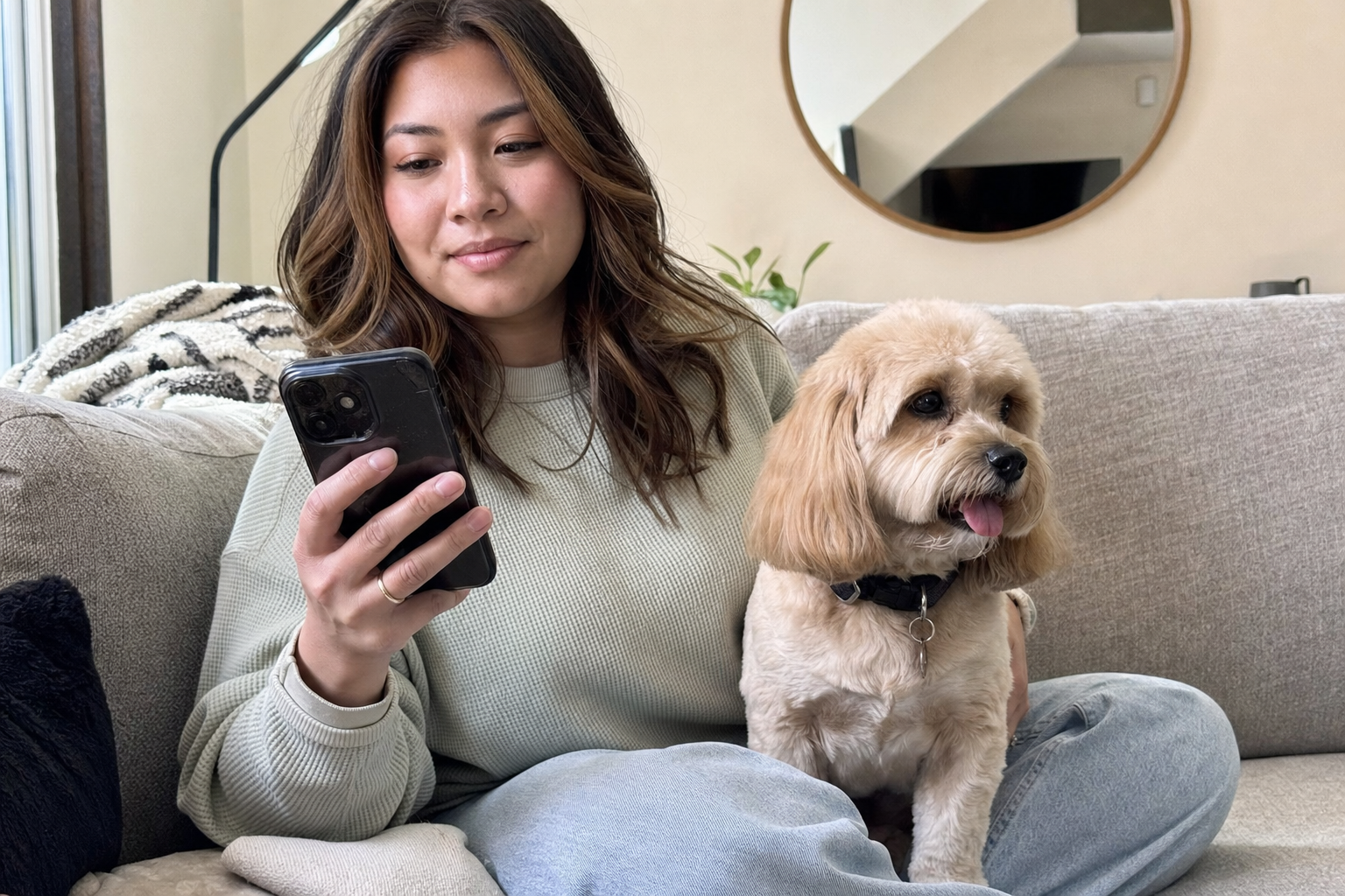 Pet owner on couch with freshly groomed dog, appearing to write a review on her phone
