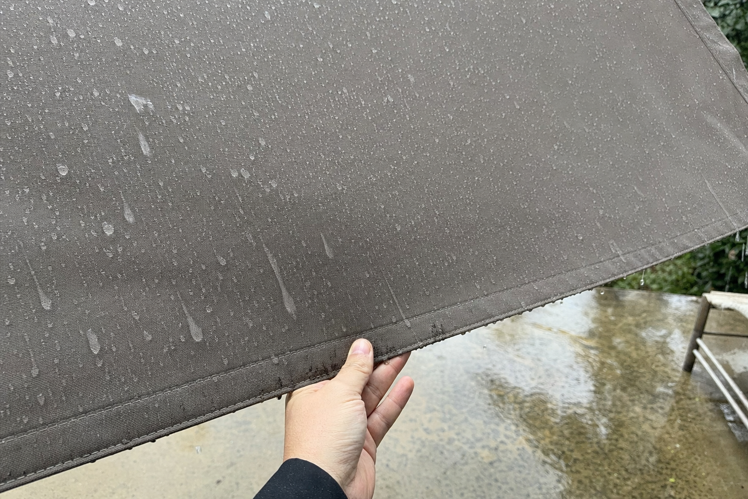 Water beading on solution-dyed acrylic awning fabric during light rain, hand testing fabric tension