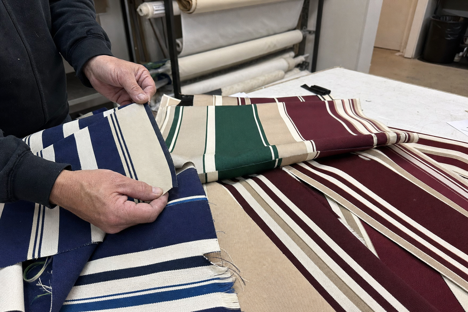 Solution-dyed acrylic awning fabric swatches in multiple colors and stripe widths laid on a worktable, hands examining the weave