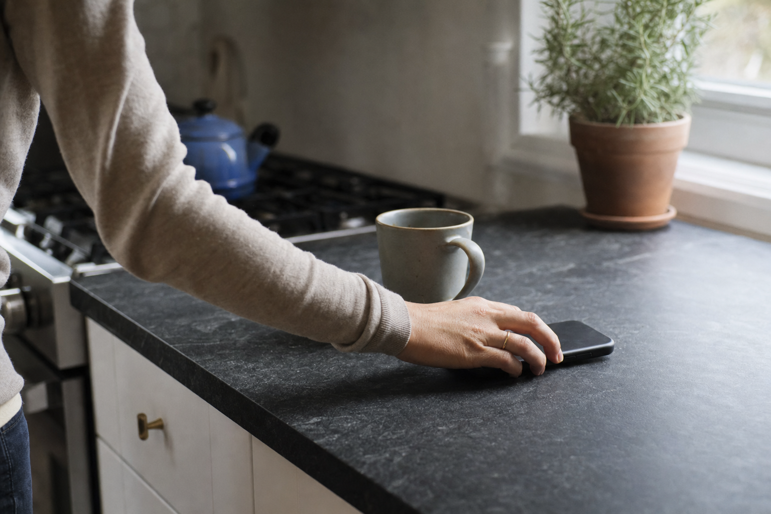 A nanny placing her phone face down on a kitchen counter next to a mug during the work day.